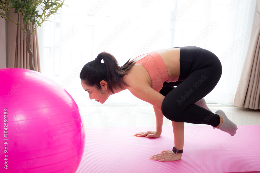 Fototapeta premium Young asian woman in activewear practicing yoga on mat in living room at home, woman practicing workout with strength and strong of arm and hand, sport for flexibility and wellness, one person.