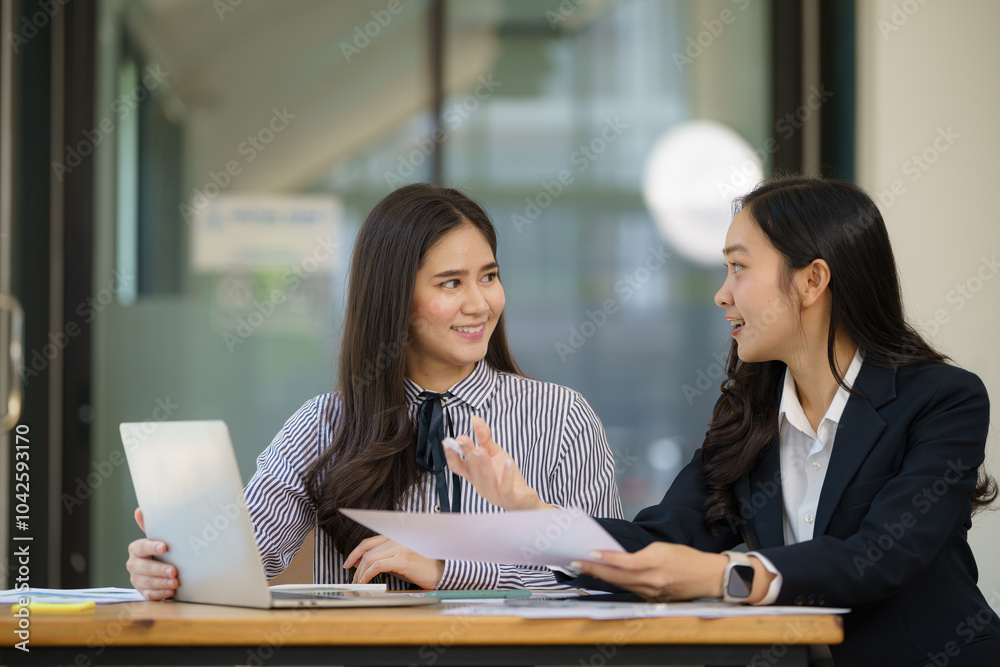 Two young Asian businesswomen discussed investment project work and planning strategy. Business people talk together on laptop computers at the office. Two young Asian businesswomen discussed investment project work and planning strategy. Business people talk together on laptop computers at the office.