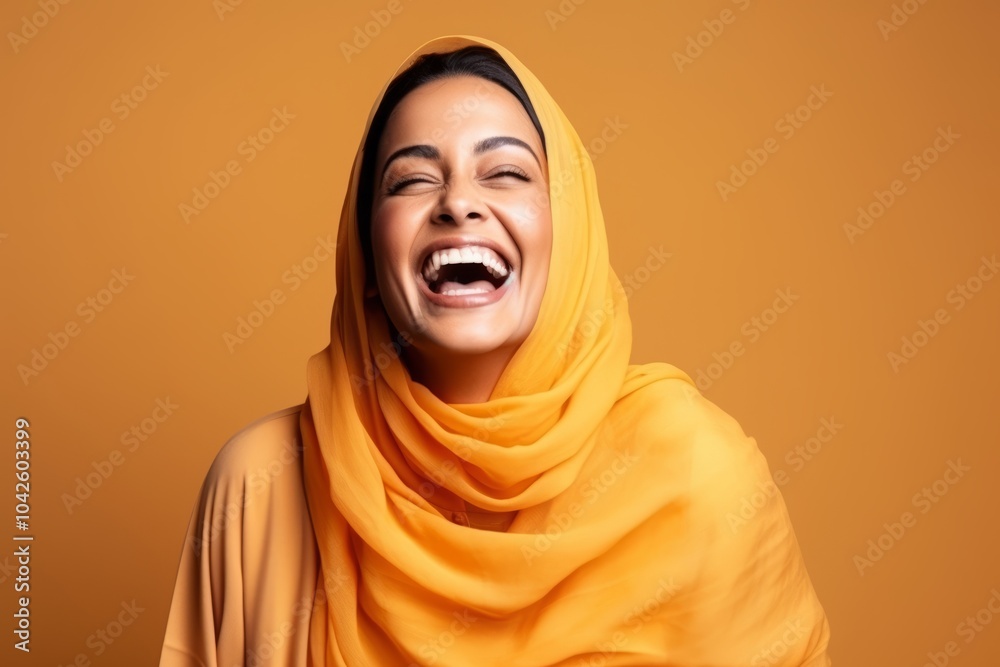 Portrait of a beautiful young muslim woman laughing against orange background Portrait of a beautiful young muslim woman laughing against orange background