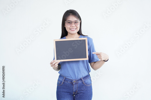 Beautiful Asian woman smiles while holding a blank blackboard, ready for promotion against a white background