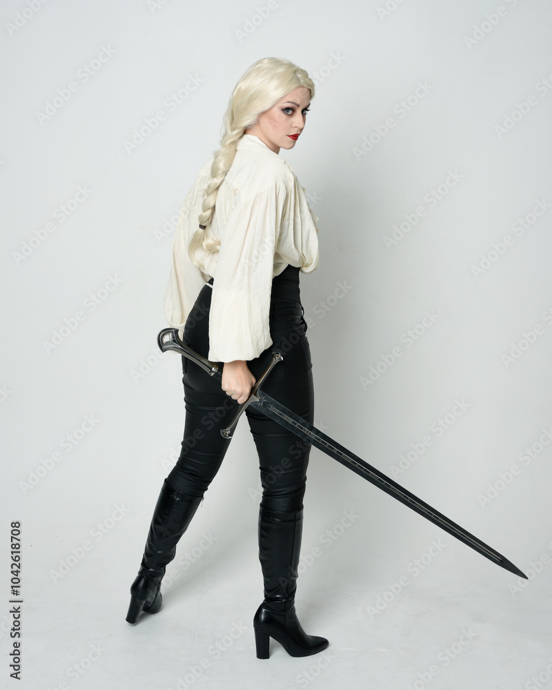 Full length portrait of beautiful female model wearing vintage gothic fantasy blouse, leather pants, boots and blonde plaited hair, larp costume. standing pose housing sword weapon in fighting action Full length portrait of beautiful female model wearing vintage gothic fantasy blouse, leather pants, boots and blonde plaited hair, larp costume. standing pose housing sword weapon in fighting action