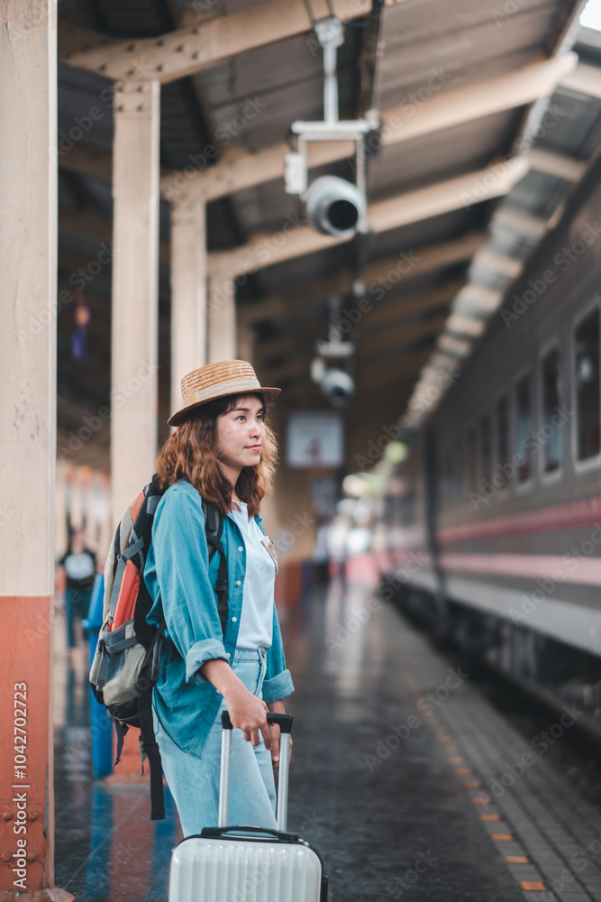 Obraz premium A young woman with a suitcase and backpack waits at a train station, ready for her next travel adventure.