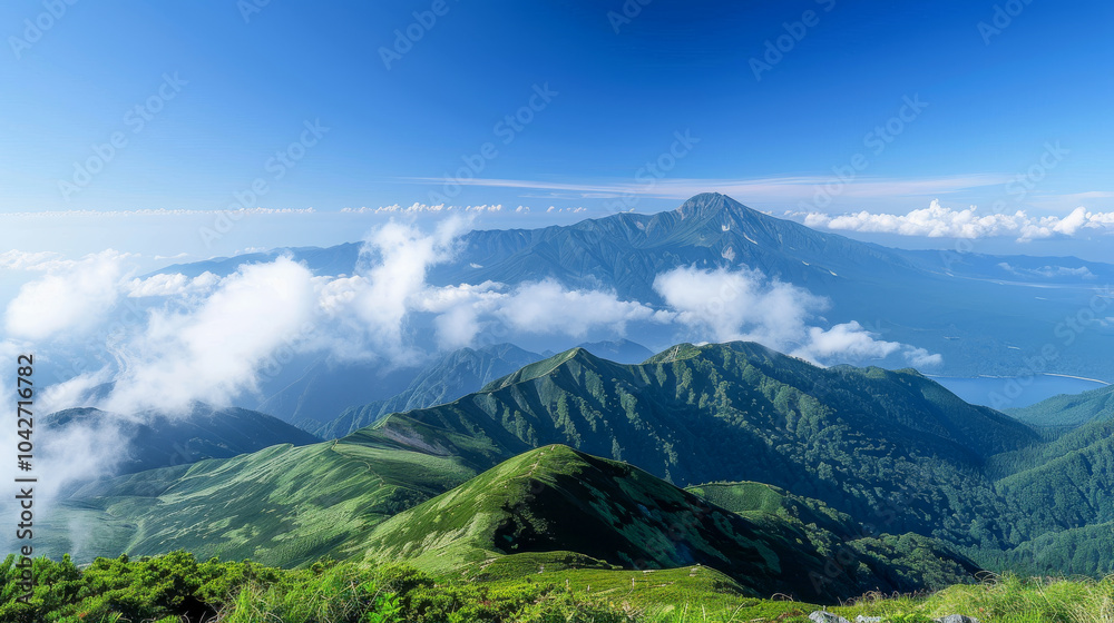 Fototapeta premium Lush green mountains under a clear blue sky with scattered clouds creating a peaceful and serene atmosphere
