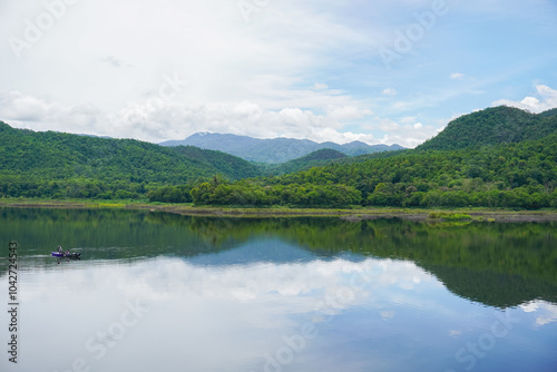 A beautiful nature landscape of the greenery mountains, blue sky, and clouds reflect on a calm water. A symbol of a relaxing holidays, nature, countryside, forest, camping site, calm, and stillness