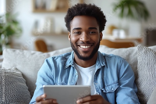 Smiling african american man using digital tablet while sitting on couch at home photo