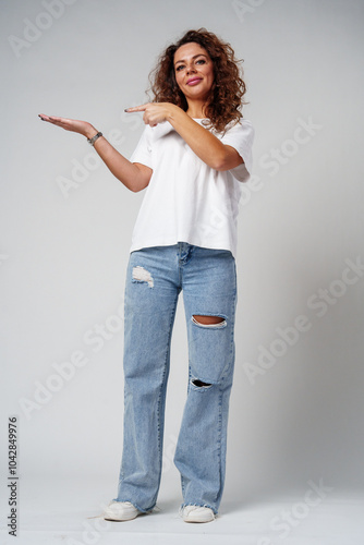 A young woman with curly hair playfully pointing finger while standing against a gray background