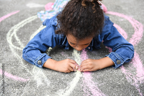 Child lying on pavement, focused on drawing with chalk, denim ja photo