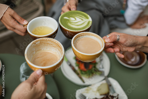 Four friends gather for breakfast and toasting with cups of coffee, buckwheat tea and matcha latte on the summer terrace.