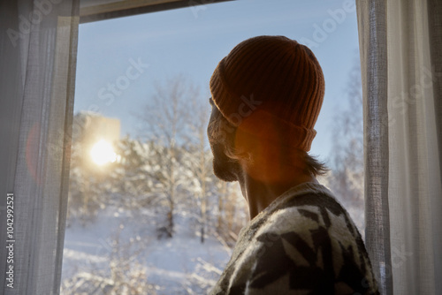 Side view of man wearing beanie while looking through window at home photo