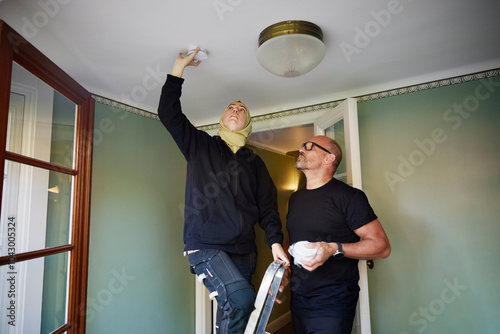 Man standing near woman installing smoke detector on ceiling at home
