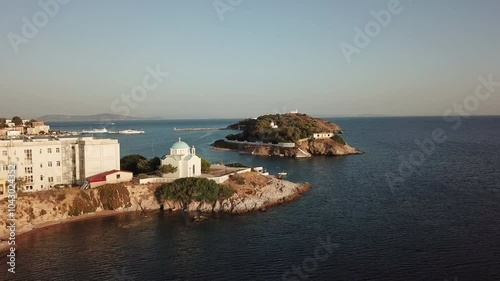 Greece,Ionusses Island, Drone Footage starts from the chapel with blue dome , turns around the bay and moves towards to the harbor and the town spread to the hill. sailboats by the harbor, calm sea. photo