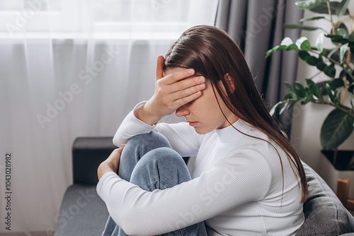 Worried sad young caucasian woman sitting alone on couch at home thinking pondering, anxious unhappy brunette female suffer from mental psychological personal problems mourn or yearn concept