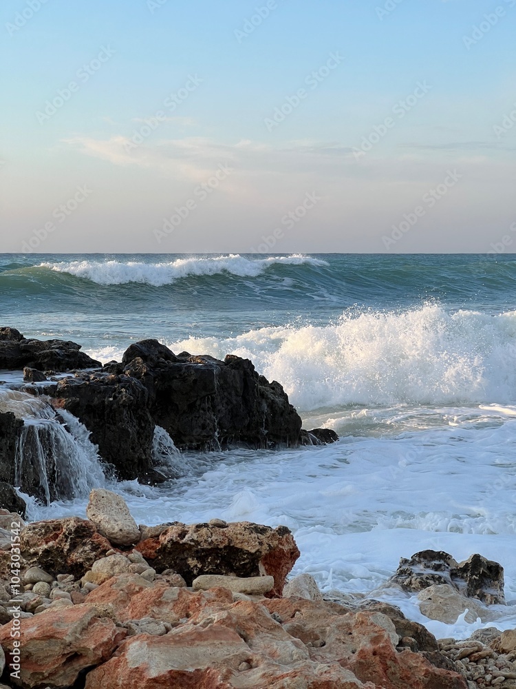 Waves crashing against rocky shore under a calm evening sky Waves crashing against rocky shore under a calm evening sky