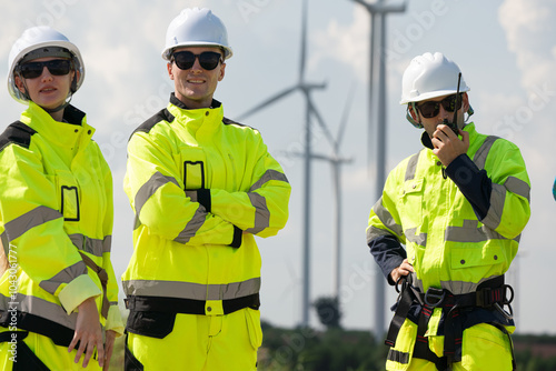 Maintenance engineer team standing at windmills at wind turbine farm. Skill people working outdoors at alternative renewable energy wind power station. Sustainable clean energy technology. Ecology