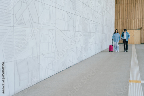 Wallpaper Mural Young adult Caucasian couple walking in modern airport terminal with pink suitcase. Male and female wear casual clothing relaxed and comfortable, architectural design on background. Torontodigital.ca