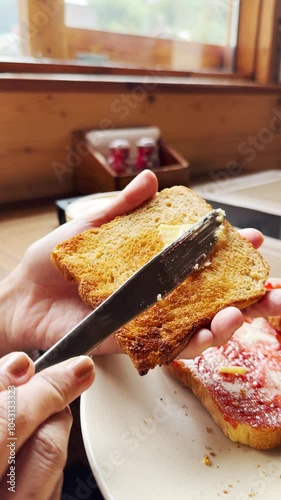 Close up shot of girl hand holding bread and applying butter with knife. Hand holding knife spreading butter on toast. Morning breakfast. 4K vertical video.
 photo