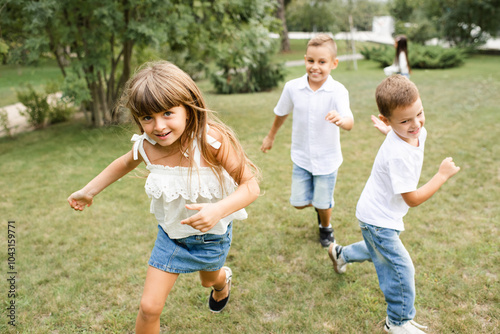 Cute stylish group of children 5 - 6 year old wearing denim clothes running on green grass lawn in park. Happiness. Childhood. photo