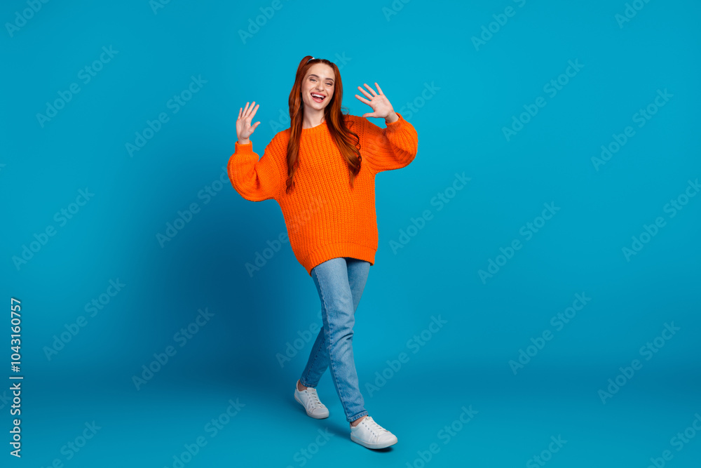 Full body photo of attractive young woman walking wave hand dressed stylish knitted orange clothes isolated on blue color background Full body photo of attractive young woman walking wave hand dressed stylish knitted orange clothes isolated on blue color background