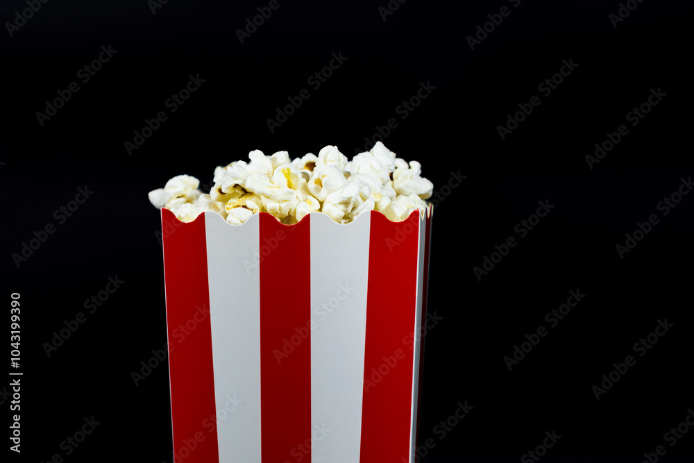Popcorn in a red and white cardboard bucket on a black background close up image, cinema food and entertainment concept Popcorn in a red and white cardboard bucket on a black background close up image, cinema food and entertainment concept