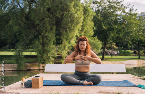 Woman practices Sukhasana by the lake in a serene park photo