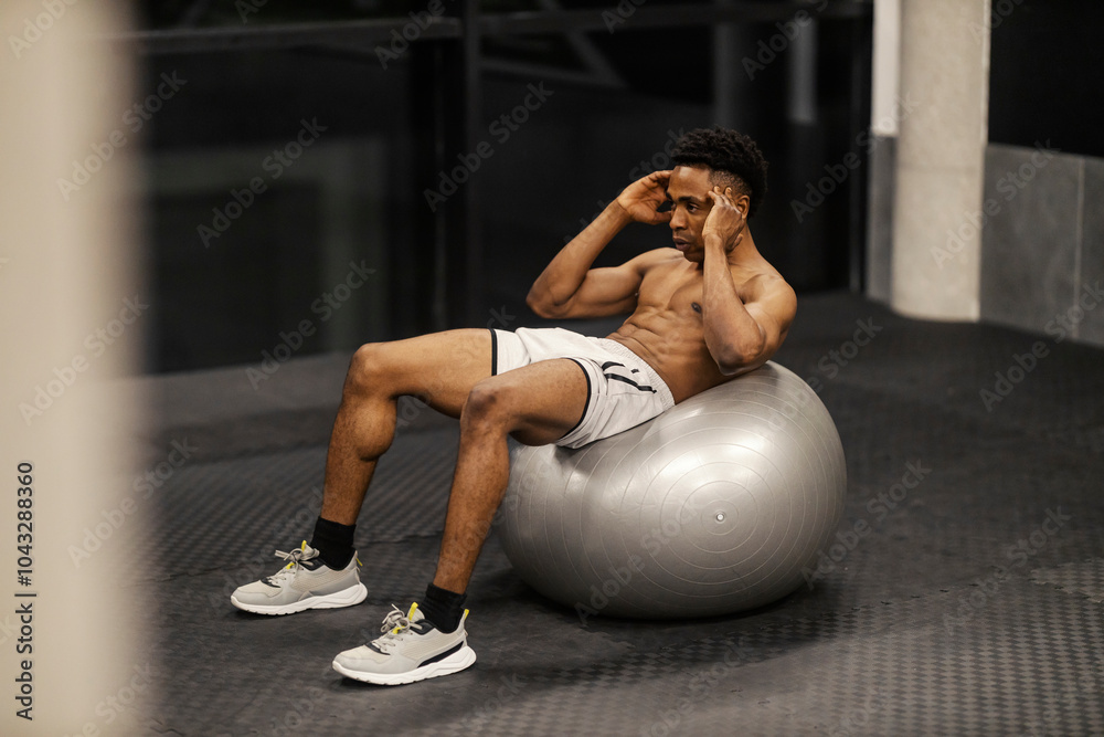 Naklejka premium Strong muscular shirtless diverse sportsman doing crunches on fitness ball at gym.