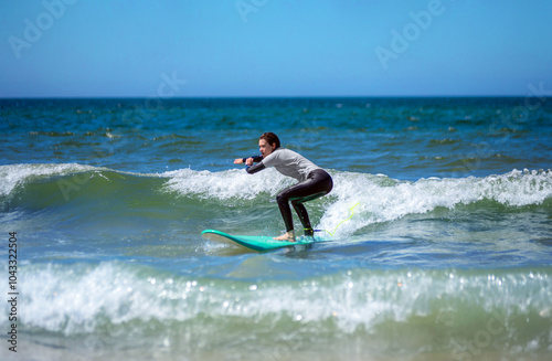 Teenage girl learning to surf on foam in the ocean. First surfing lesson. Amateur surfer. Surfing training. Photo for surfing school advertising on social media.