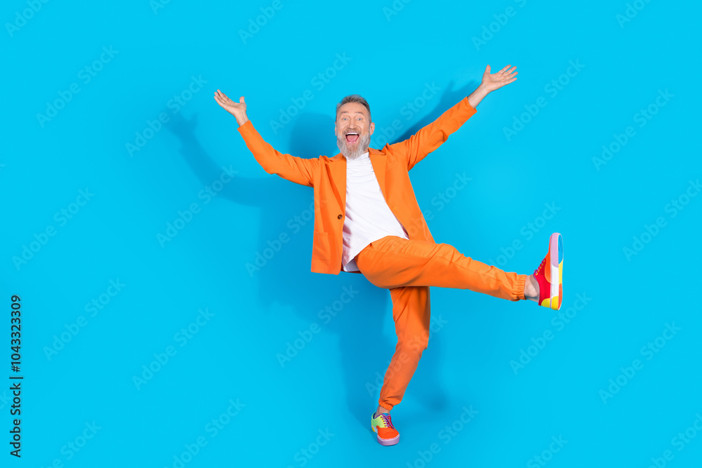 Full size photo of funny trendy aged man dancing empty space wear orange costume isolated on blue color background Full size photo of funny trendy aged man dancing empty space wear orange costume isolated on blue color background