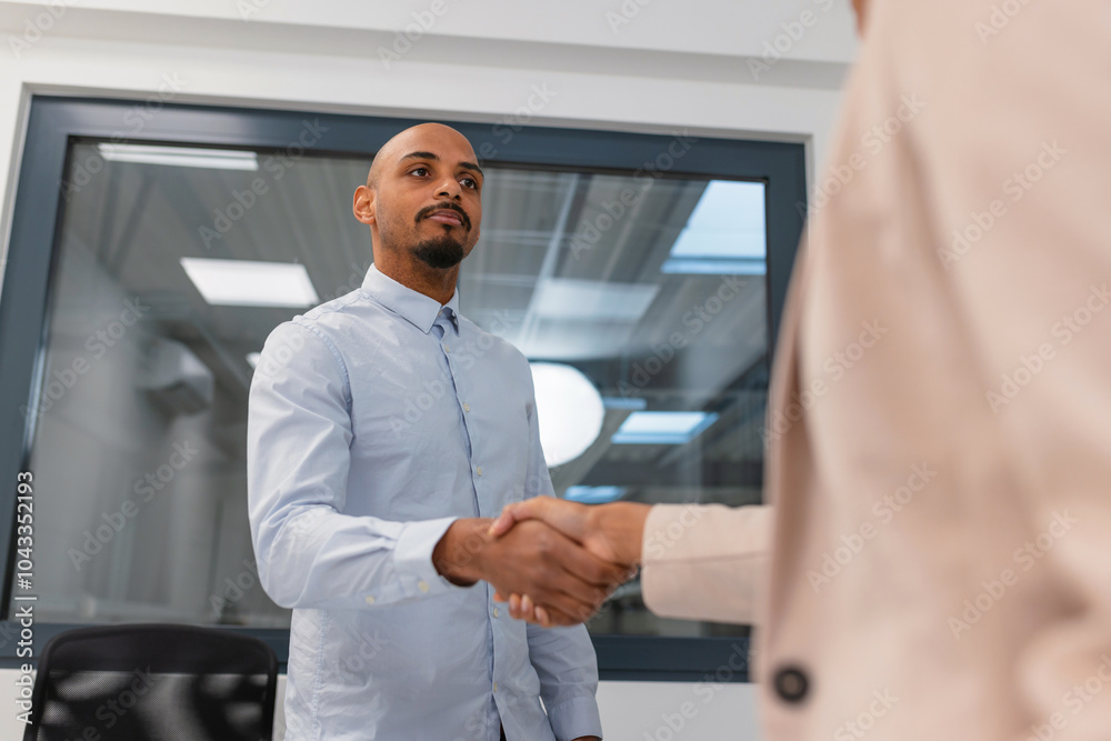 Fototapeta premium Dynamic young Indian woman, a seasoned company manager, handshaking with a promising African American job applicant, after an employment interview.
