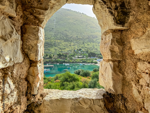 Picturesque view framed by stone window of watching tower of Porto Palermo fortress in Vlore, Albania. Vista reveals serene bay with turquoise Ionian sea surrounded by lush greenery and rolling hills photo