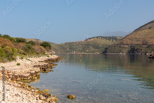 Scenic view of Porto Palermo Bay surrounded by majestic Ceraunian mountain range in Vlore, Albania. Calm turquoise Ionian Mediterranean sea stretches out towards small peninsula with fortress atop photo