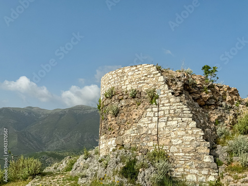 Ruins of an ancient stone building in Himare Castle, Vlore, Albania. Meadow of wildflowers blooming with scenic view of Ceraunian mountain range. Partially collapsed walls of historical site. Discover photo