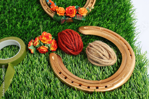 Horseshoe has been used and spray painted gold. Rolls of red, brown hemp rope, artificial flowers and a roll of green masking tape All placed on artificial grass.

 photo