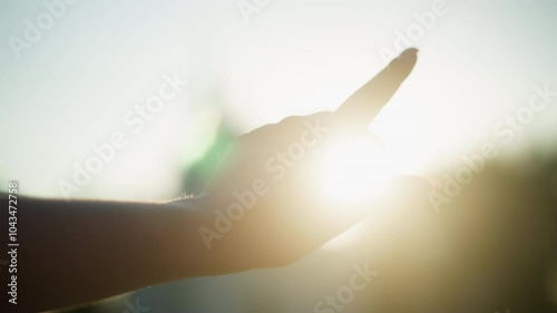 Close up of hand reaching towards bright sunlight, creating captivating interplay between fingers and warm sun rays, with blurred background