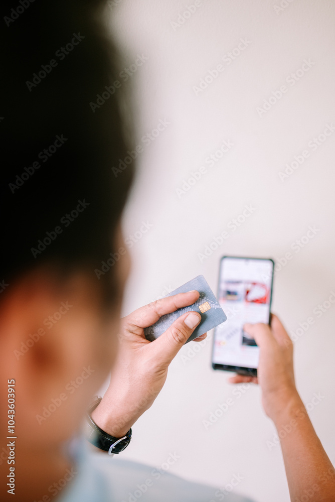 A Southeast Asian man is shopping online, using his debit card for a seamless transaction. A Southeast Asian man is shopping online, using his debit card for a seamless transaction.