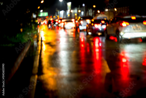 A blurry image of a busy street at night with cars and a few pedestrians. The image has a moody and somewhat chaotic feel to it, as the cars are moving quickly and the rain is making the street slick photo