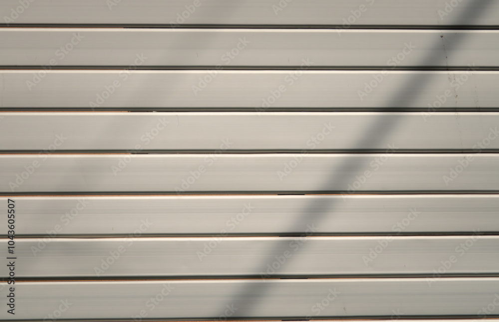A white wall with a series of wooden slats. The slats are arranged in a way that creates a shadow on the wall, giving the impression of depth and texture A white wall with a series of wooden slats. The slats are arranged in a way that creates a shadow on the wall, giving the impression of depth and texture
