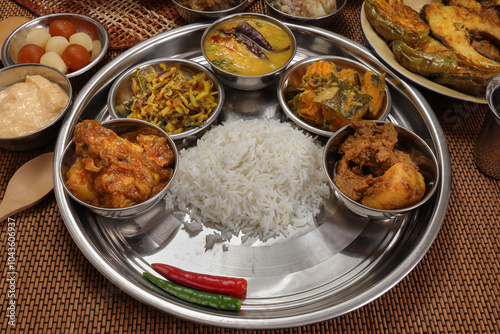 Bengali style thali spread verity cuisine hilsa fish vegetable beef mutton egg curry fry vorta mashed chicken liver sweet yogurt side dish served on rustic metal tin stainless steel plate small bowls photo