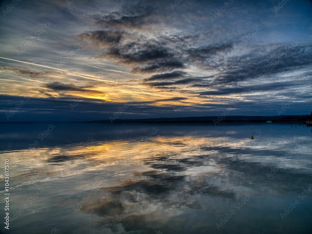 Obraz premium Sunset over calm lake with reflections.