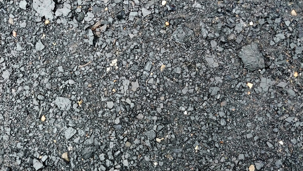 a close-up view of an asphalt surface. The texture is rough and uneven, with small stones and gravel embedded in the dark, tar-like material a close-up view of an asphalt surface. The texture is rough and uneven, with small stones and gravel embedded in the dark, tar-like material