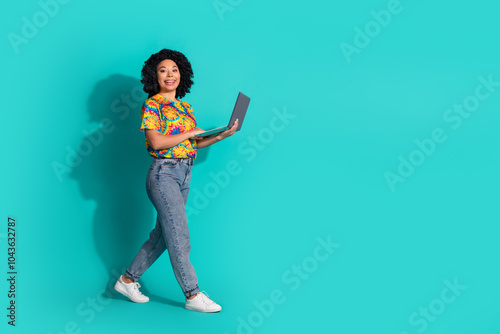 Full length photo of charming positive woman wear print t-shirt working modern device walking empty space isolated teal color background