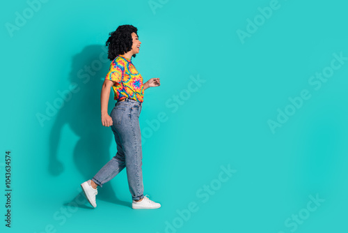 Full length photo of adorable lovely girl wear print t-shirt walking empty space isolated turquoise color background photo