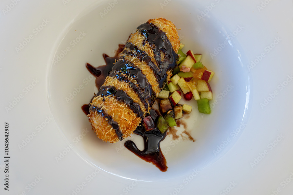 Fried ice cream with shredded wheat, fruit pieces and chocolate sauce on a white porcelain plate (Hot ice cream)