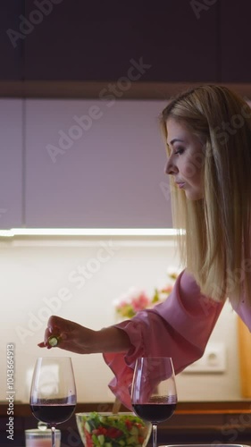 Lady drink spiker pours soporific powder into glass with red wine of lover and looks into camera before romantic dinner in kitchen slow motion photo