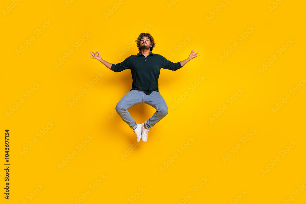 Obraz premium Young man in a black shirt and jeans jumping joyfully against a bright yellow background on a casual friday
