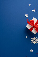 White vertical gift box with a striking red ribbon surrounded by decorative snowflakes on a blue background, creating a festive and elegant Christmas atmosphere