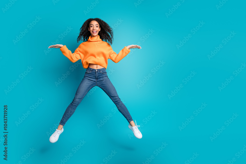Full length photo of cheerful pretty teen lady dressed orange turtleneck jumping high comparing arms empty space isolated blue color background Full length photo of cheerful pretty teen lady dressed orange turtleneck jumping high comparing arms empty space isolated blue color background