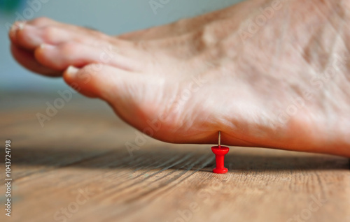 A person's barefoot stepping on a red pushpin tack photo