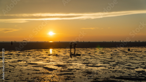 Group walking on beach during sunset, admiring red sky at dusk over water