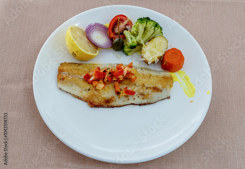 Obraz na płótnie Grilled sea bass in a white porcelain plate. Garnish: lemon, onion, tomato, capers, broccoli, potatoes, carrots. w salonie