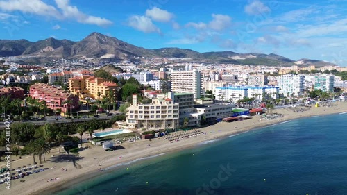 Drone flight over the Benalmadena coast overlooking the coastline, beach, residential sector and mountains in the background.